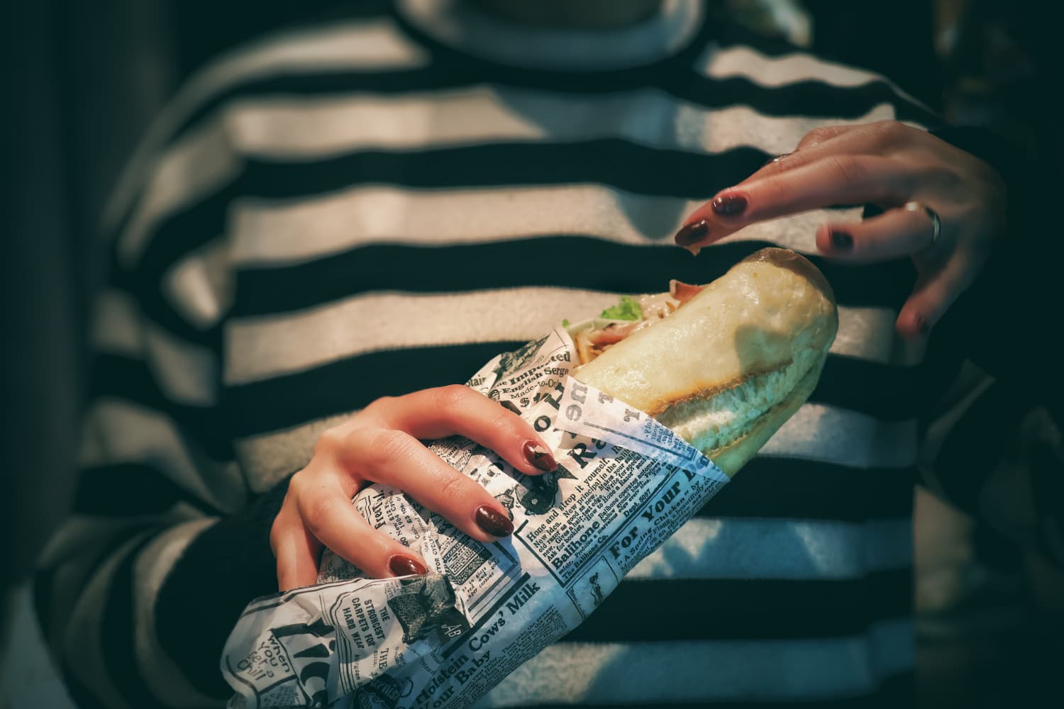 Hands holding a paper-wrapped sandwich in soft light