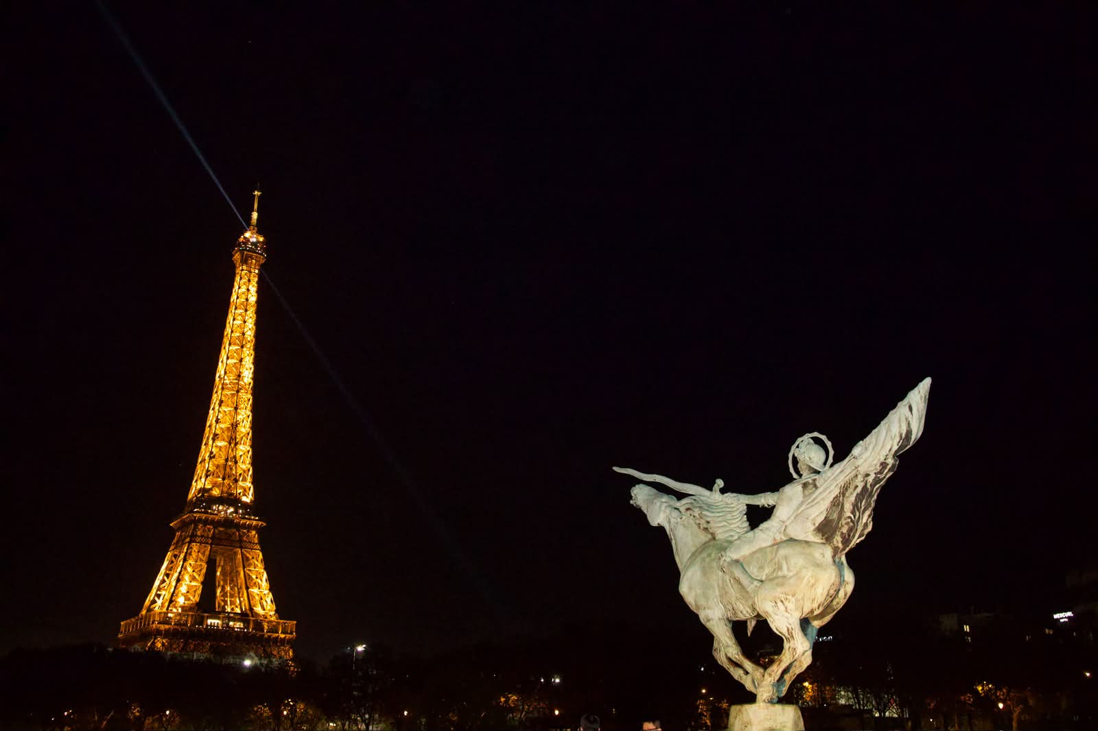 Eiffel Tower glowing beside a winged statue at night